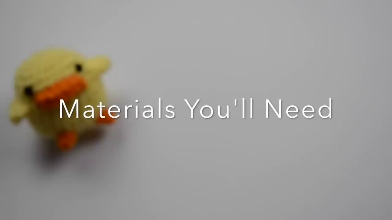 A close-up of the essential beginner's crochet toolkit: a 5.0mm hook, light-colored worsted weight yarn, and a pair of scissors.