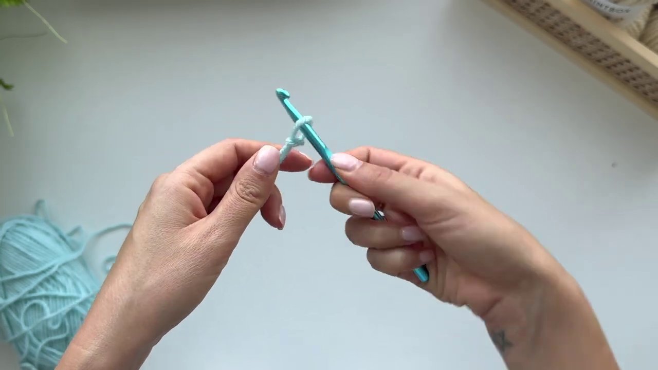 A clear shot of the hand holding a crochet hook using the knife grip, with the thumb positioned on the flat grip.