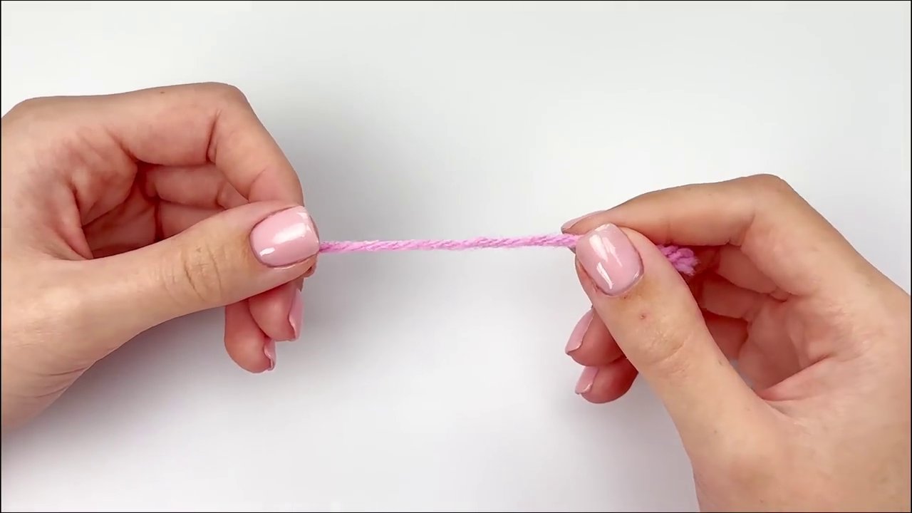 Demonstrating how to create a slipknot by wrapping yarn around the fingers.