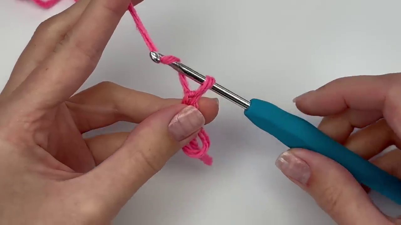 The crafter's hands demonstrating the initial steps: forming the magic circle loop around two fingers and beginning the first chain stitch.