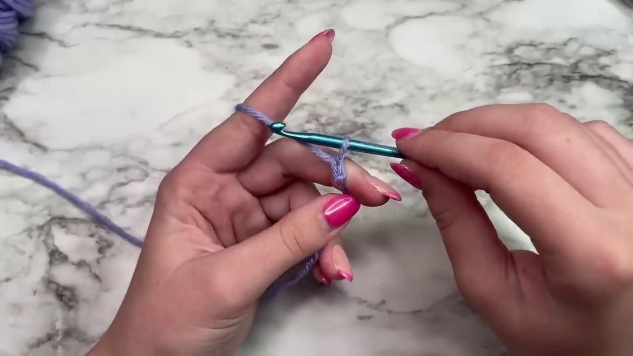 A close-up view of the hands forming the initial slip knot on the crochet hook.