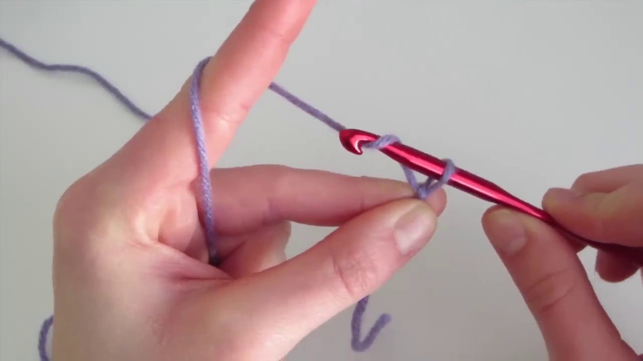 The hook is shown mid-stitch, pulling the yarn through a loop to complete one chain stitch, forming a clear "V" shape.