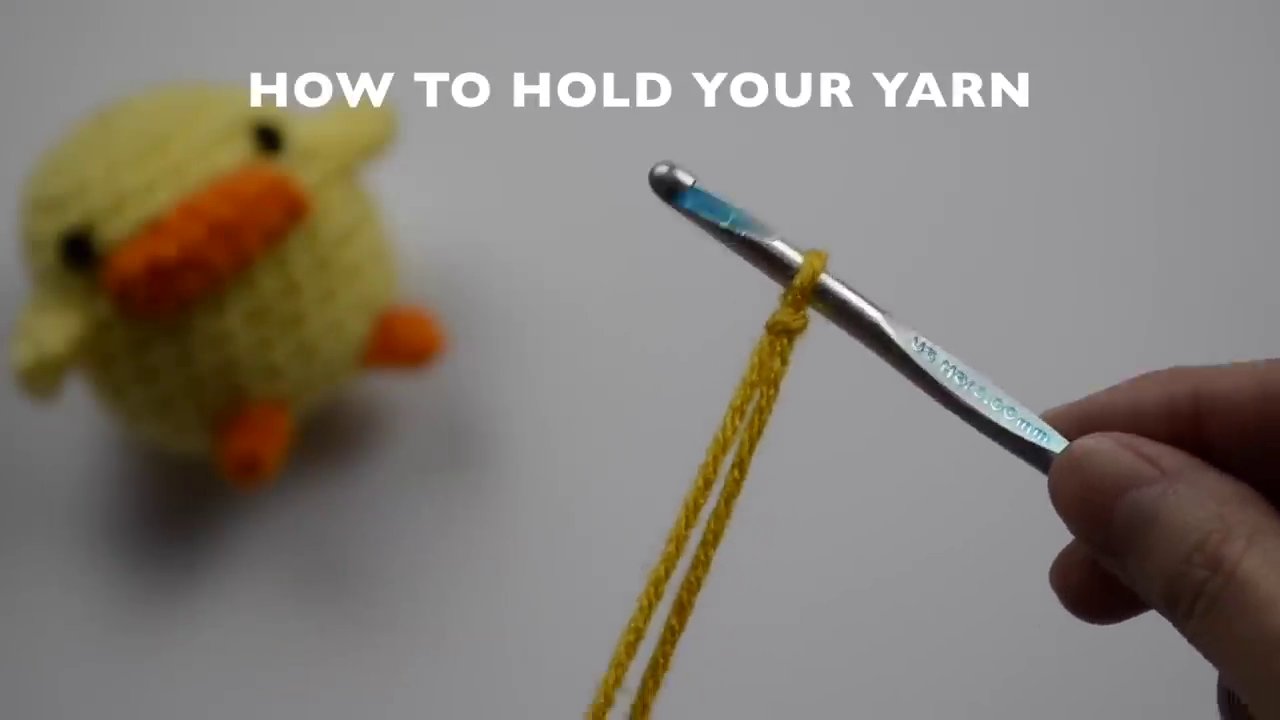 A hand demonstrating how to hold the yarn for proper tension, with the yarn woven through the fingers and over the index finger.