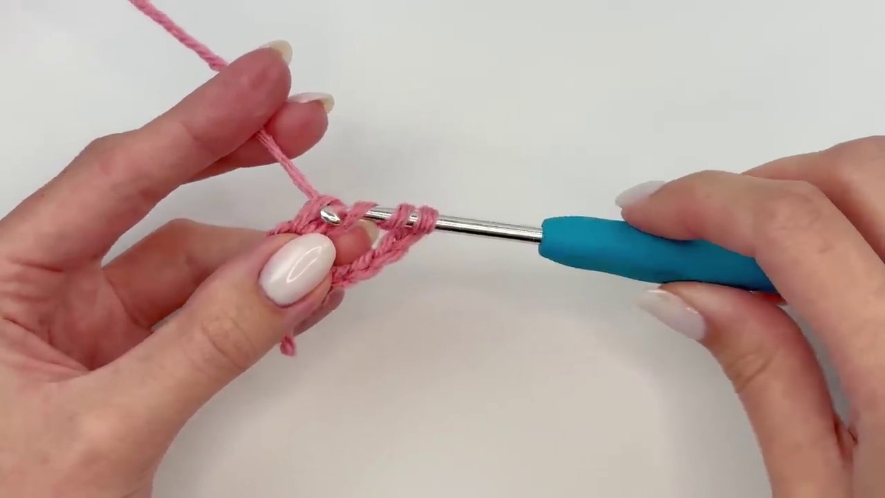 The crafter’s hands show two completed petals, with a third in progress, demonstrating how stitches are scooted down to make space.