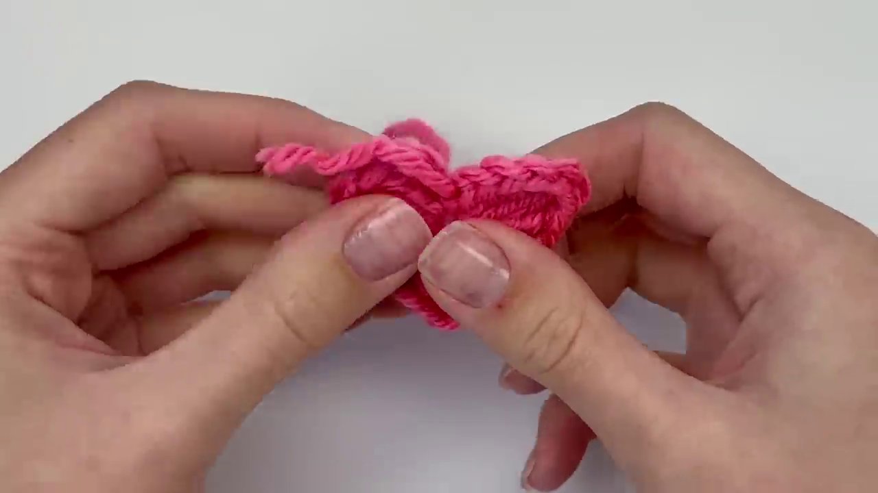 The finished, three-dimensional crochet heart held in hand, showing its perfect shape after the ends have been woven in and trimmed.