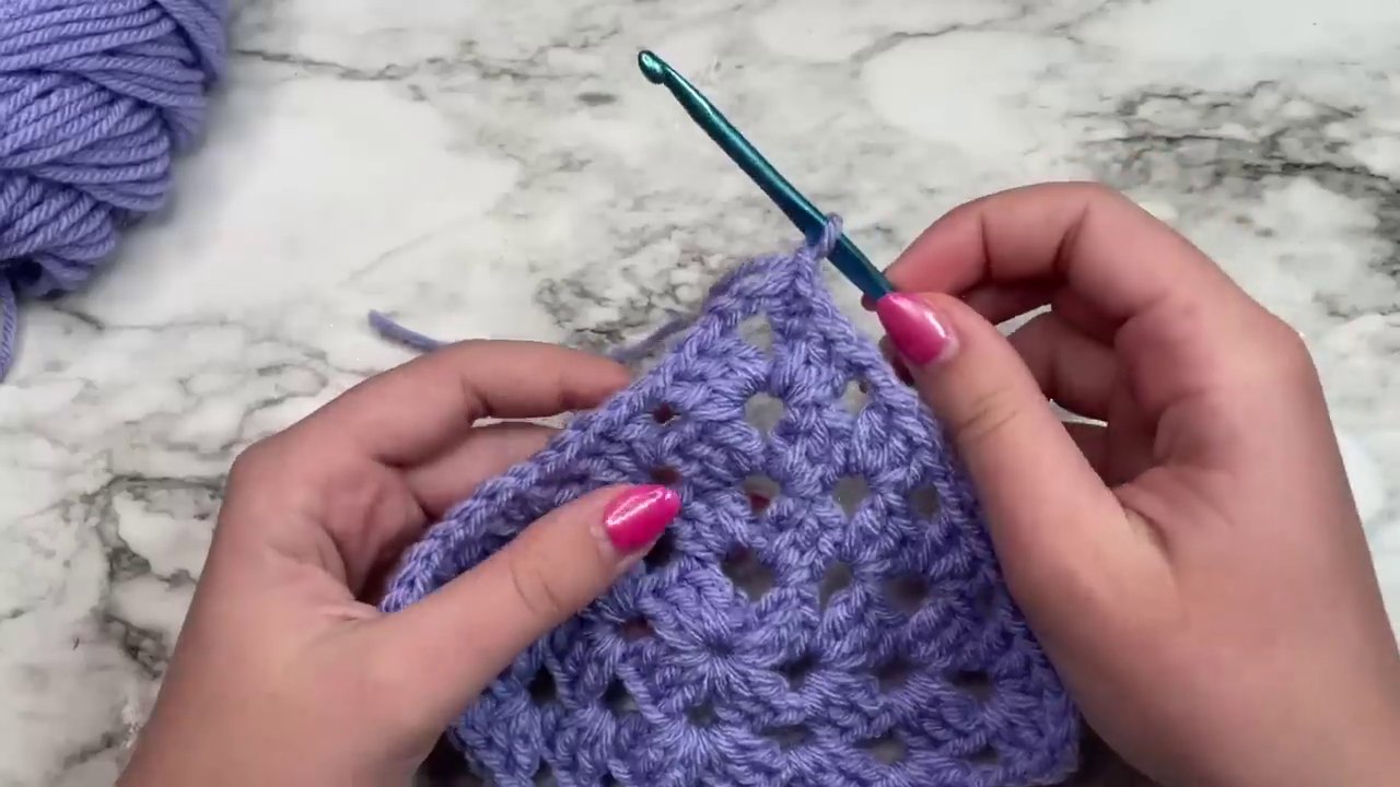 The hands weaving in the yarn tail with a tapestry needle to neatly finish the square.