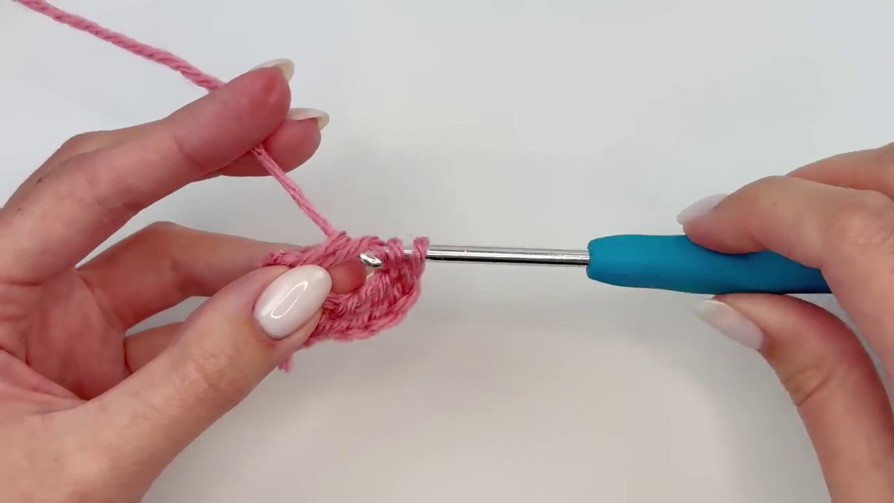 A close-up of the back of the finished flower, showing the two yarn tails being pulled tight to secure the center.