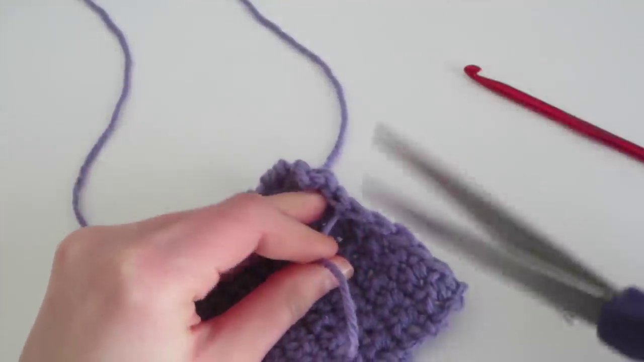 A yarn needle is used to weave the loose end back into the stitches of the finished swatch.