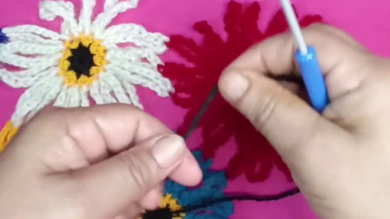 The maker’s hands holding a small black crocheted piece, with the white hook still in position.