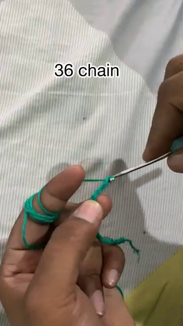 Close-up of a hand holding a crochet hook with yarn looped over the index finger.