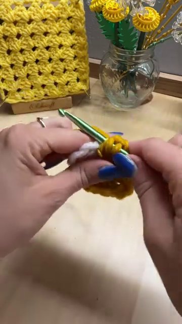 A crochet hook working three double crochets into a chain-one space between two corner clusters.