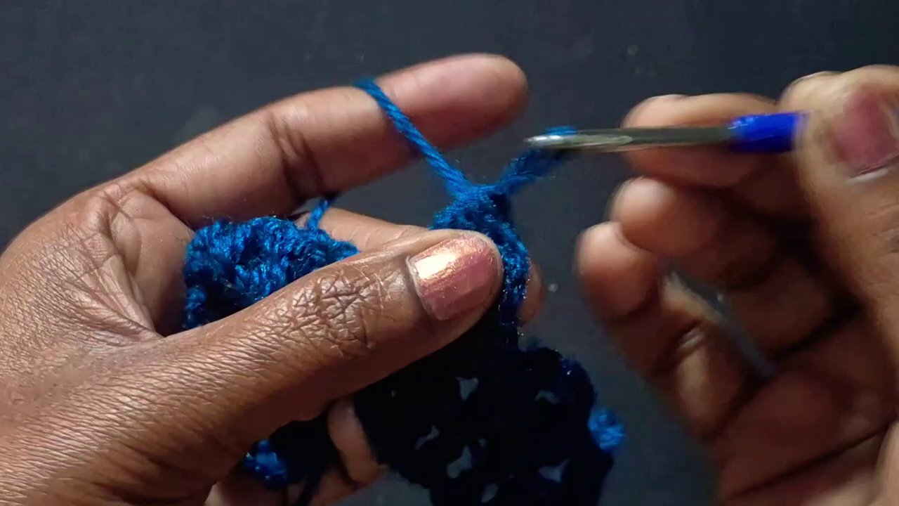A hand holding a crochet hook, working a double crochet stitch into a row of chains.