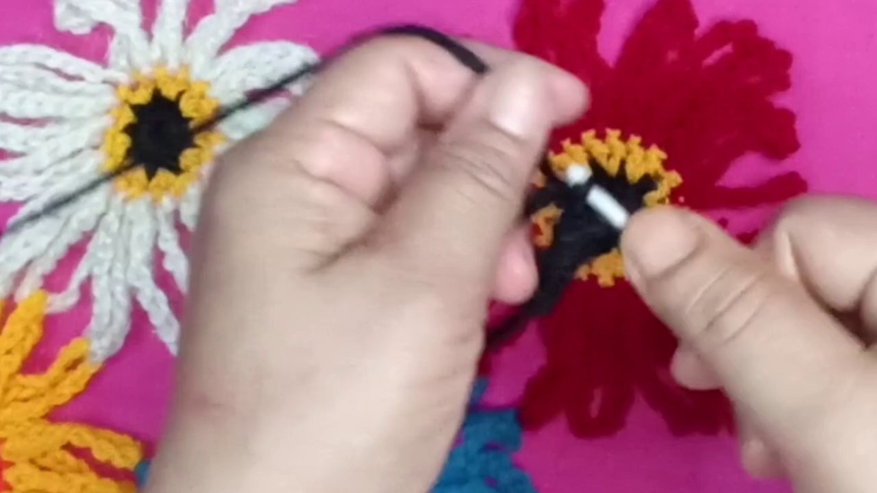 A close-up of a pink crocheted flower taking shape, with the hook and yarn clearly visible.
