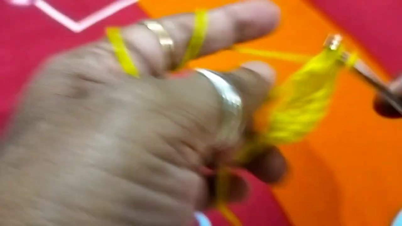The poshak body taking shape with alternating pink and yellow stripes, held in hands against the red fabric background.