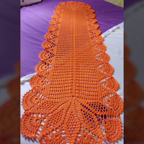 A crochet table runner with tasseled edges, draped over a console table with a framed photo and a small plant.