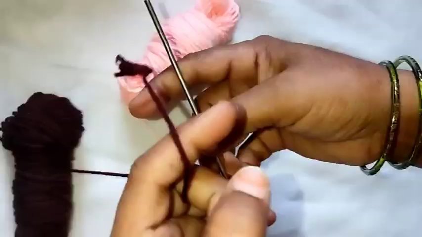 A close-up of the crochet hook looping through a stitch, with the yarn wrapped around the hook before pulling through.