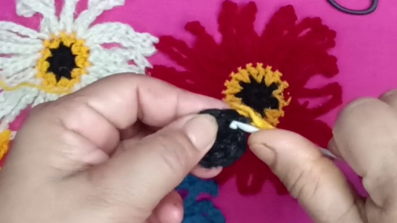 The maker’s hands working on a pink flower, with a vibrant background of completed blooms.