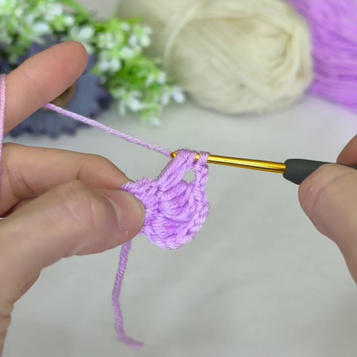 The purple yarn returns, adding a new layer of stitches around the white ring and creating a more dimensional motif.