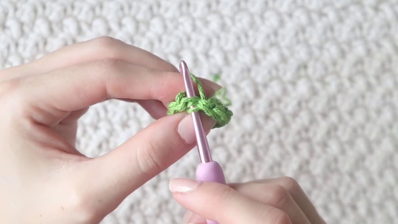 A leaf being attached to a flower stem with green thread, showing the wrapping technique.