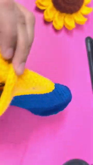 A final wide shot of the completed Minion bottle cover on the pink surface, with all tools and materials visible in the background.