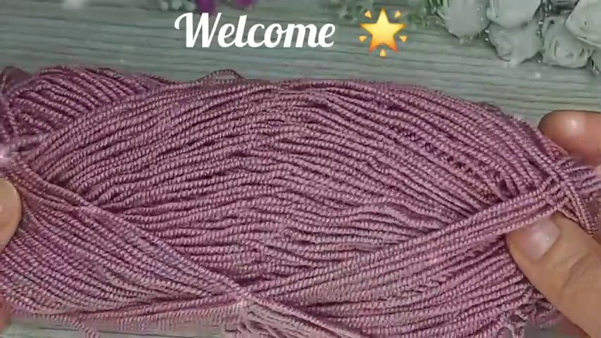 Hands holding a gold crochet hook and pink yarn, working a double crochet stitch on a light wooden surface.