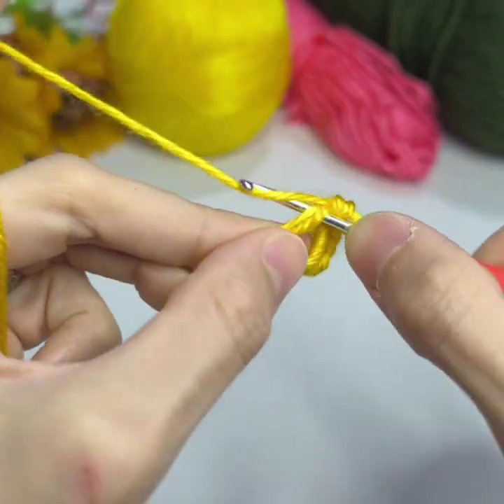 Hands form a yellow slip knot on the red-handled hook against a white table background.