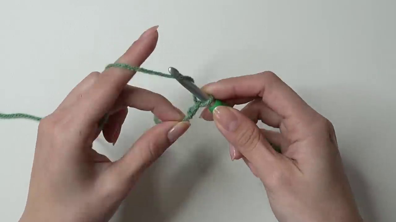 Close-up of the hook entering the tightened chain stitch, with the thumb holding it steady.
