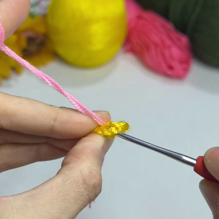 Pink yarn wraps around the hook as the first petal begins to form.