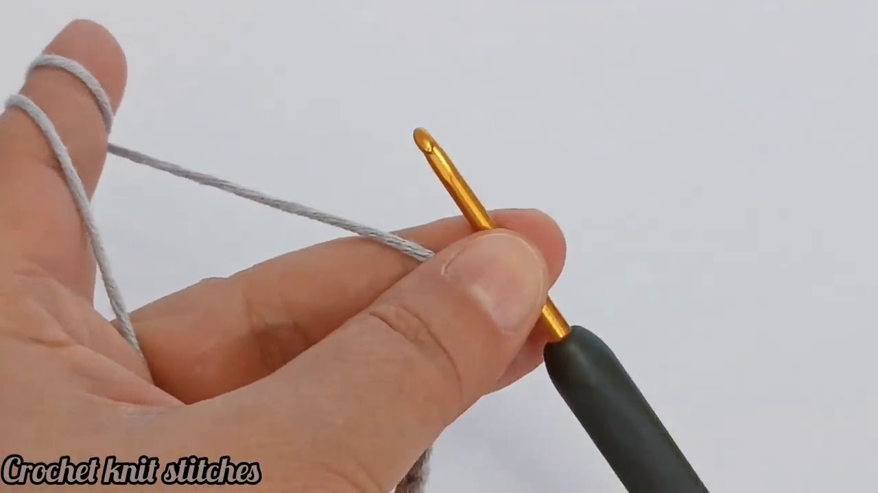 The crochet hook pulls a loop of yarn through the center of a stitch. The left hand is out of frame, and the focus is on the hook’s movement through the fabric.