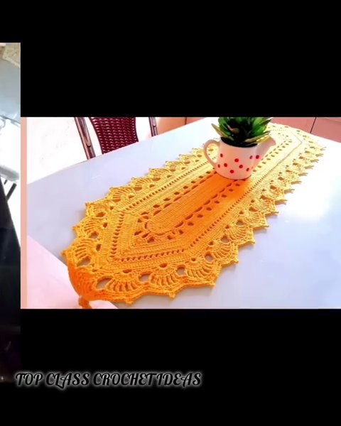 A crocheted table runner in black and gold, laid across a wooden dining table with simple white plates on top.