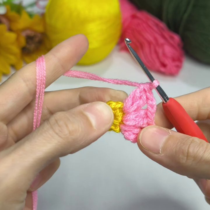 Close-up of the hook pulling pink yarn through a stitch to form a petal.