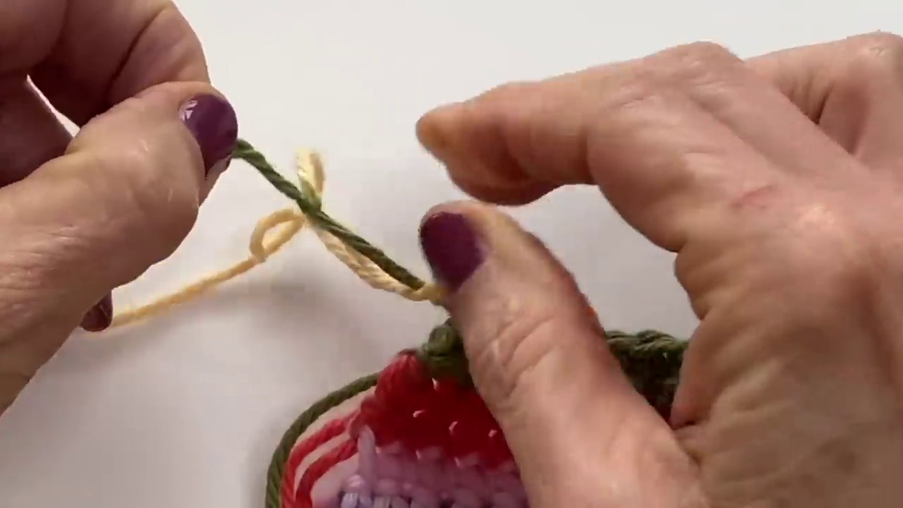 A granny square with the new color being tied in at the corner, showing the knot placement.