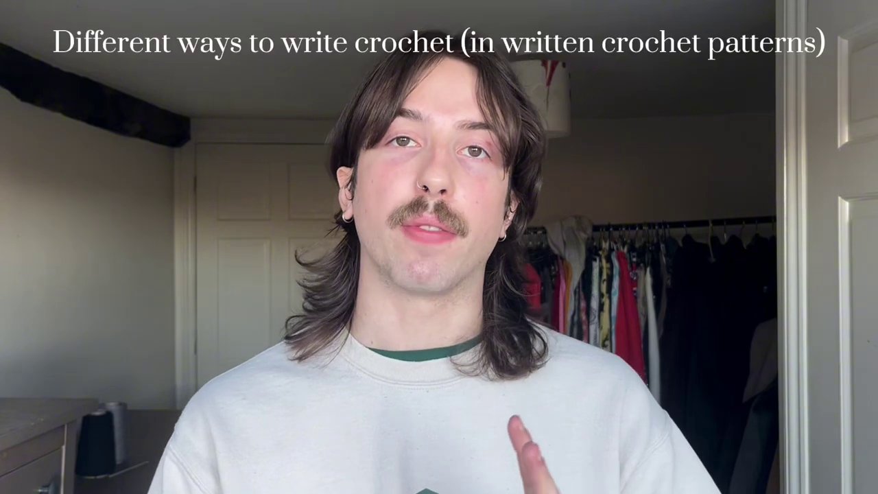 A person crocheting on a couch with a mug of tea nearby and a TV show playing in the background.