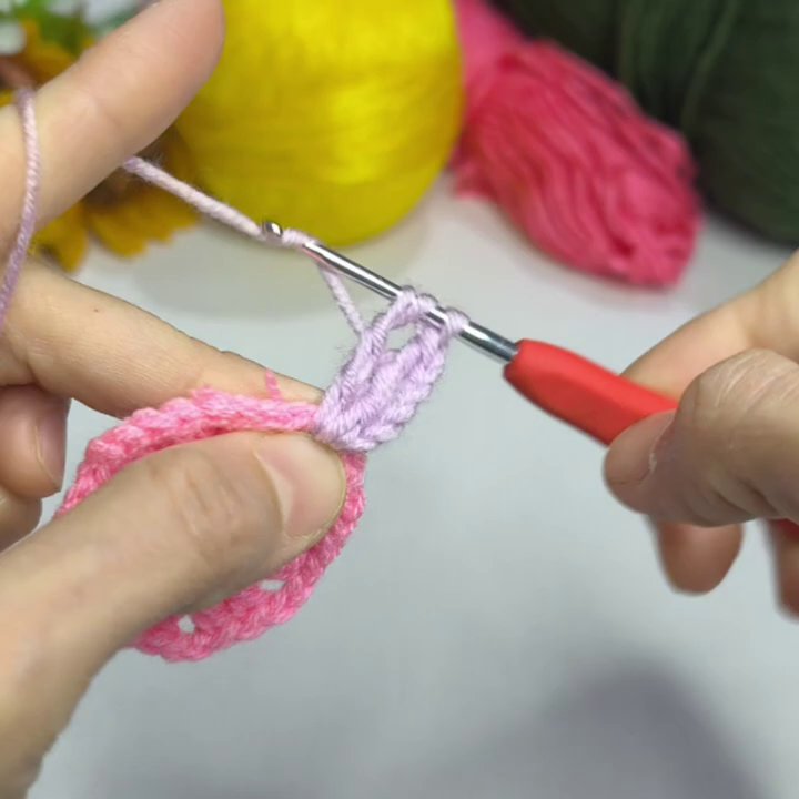 Green yarn is attached to the base of the flower to begin crocheting a leaf.