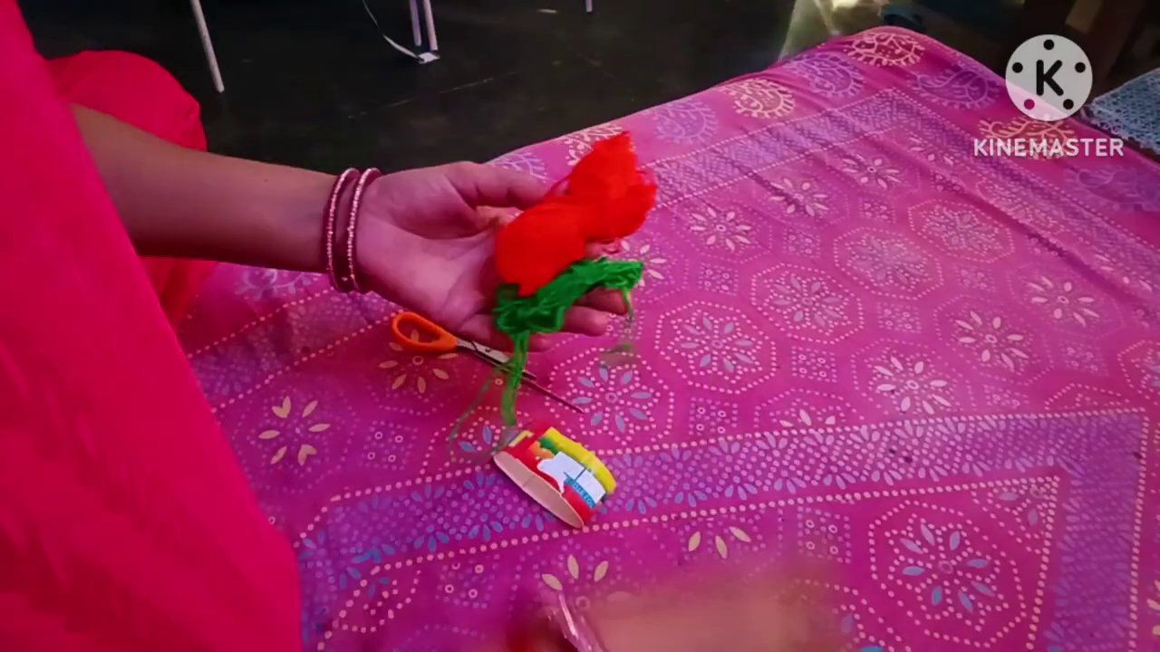 A pair of hands, bangles catching the light, holding a crochet hook and a small ball of green yarn on a floral pink fabric.