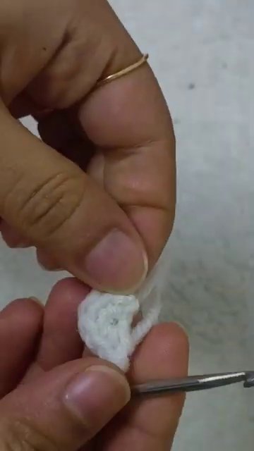 Hands holding a crochet hook and white yarn, working the first round of the base.