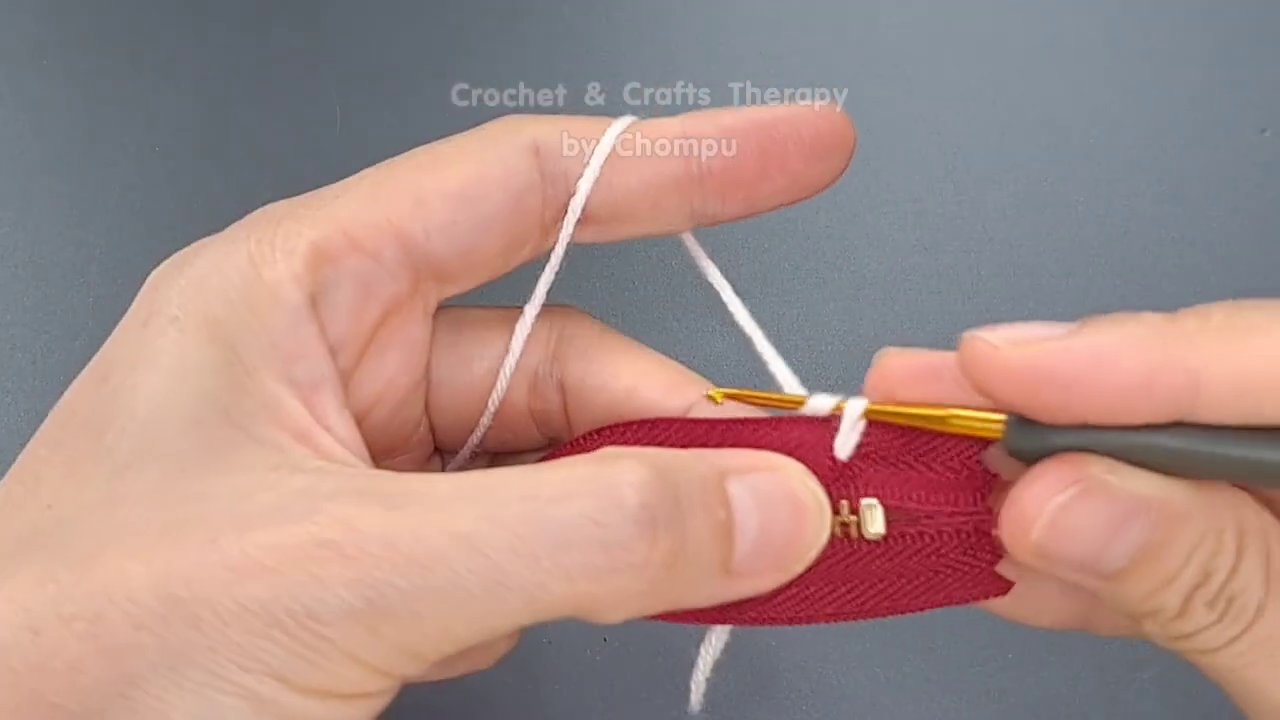 Fingers guiding the yarn and hook to create a slip stitch join along the zipper edge.