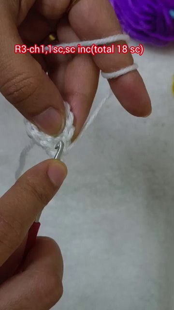 A hand switching from white yarn to a ball of purple yarn on the table.