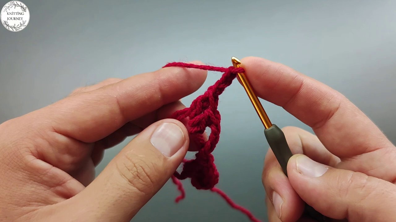 Red yarn loops forming a neat row along the stick, with the hook poised to pull through the next stitch.