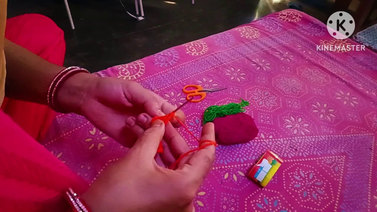 Fingers wrapping yarn around the hook, forming the first loop against the pink fabric background.
