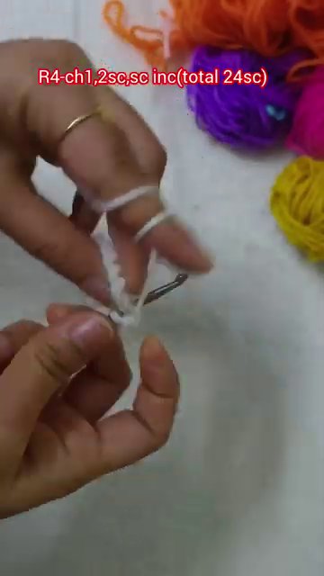 A close-up of the hook working purple yarn into a petal shape against the white base.