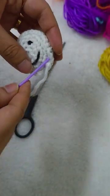 Hands attaching a silver lobster clasp to the back of the finished crochet flower.