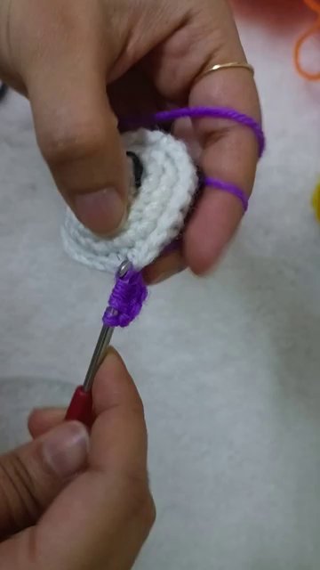A finished colorful crochet keychain resting next to a small pile of leftover yarn balls.