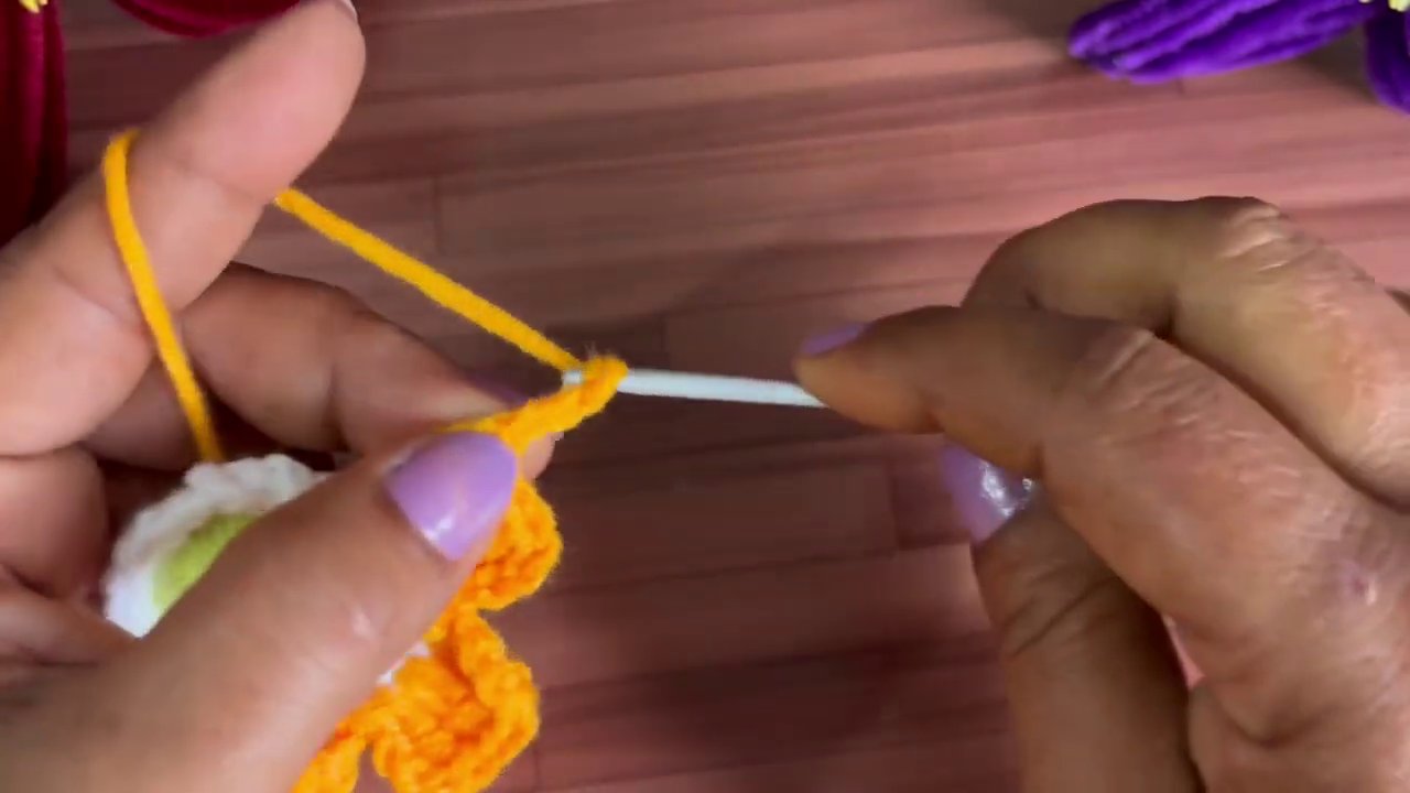 A completed crochet flower alongside red and purple versions, showing color variation possibilities.
